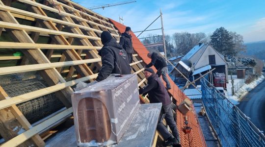 Mitarbeiter decken ein Satteldach neu ein.